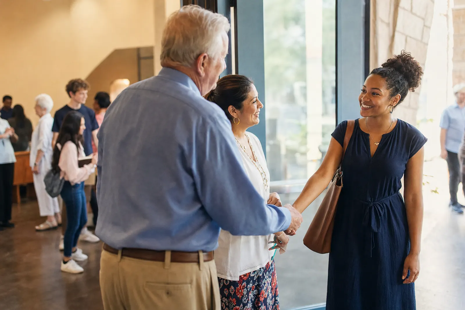 Two greeters welcome a first-time guest at the church door with a handshake.