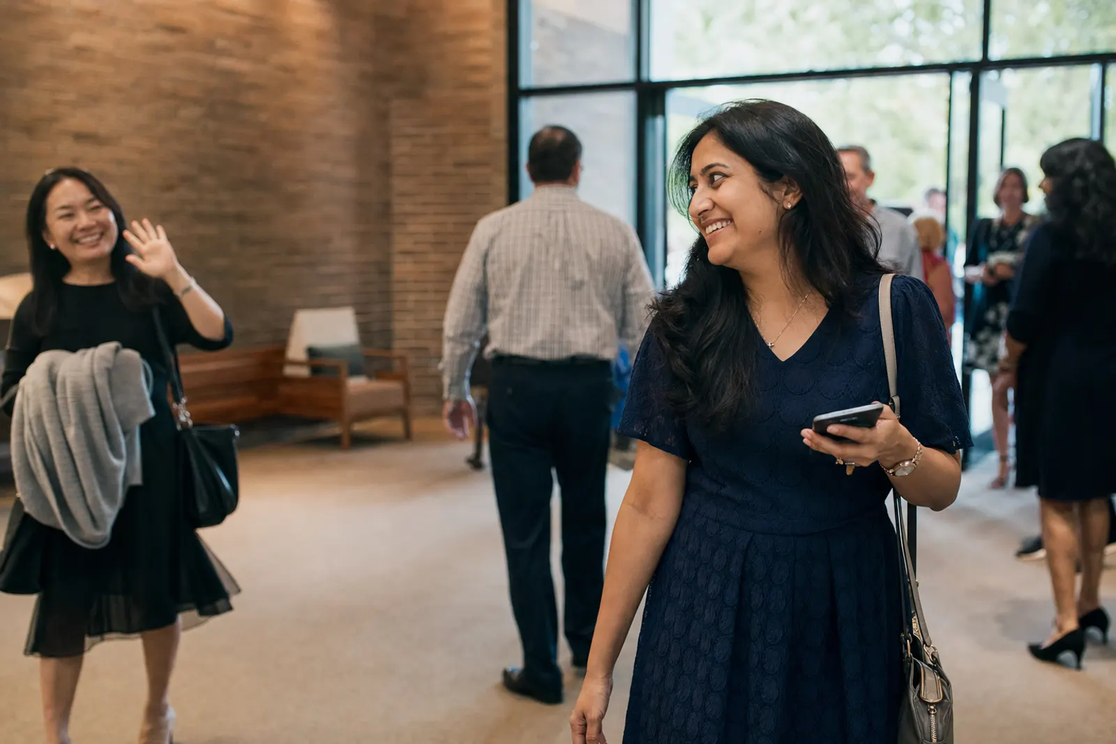 A woman walks into church with her phone as a friend waves hello.