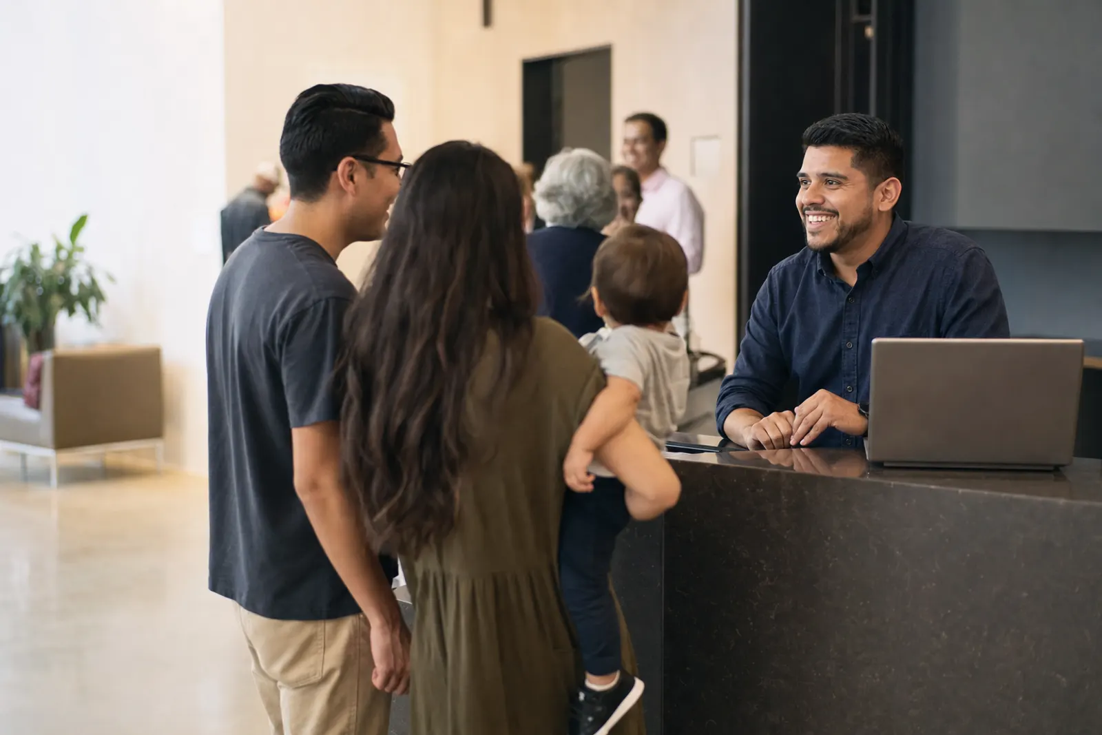A church administrator at the welcome desk greets a young family with a toddler.