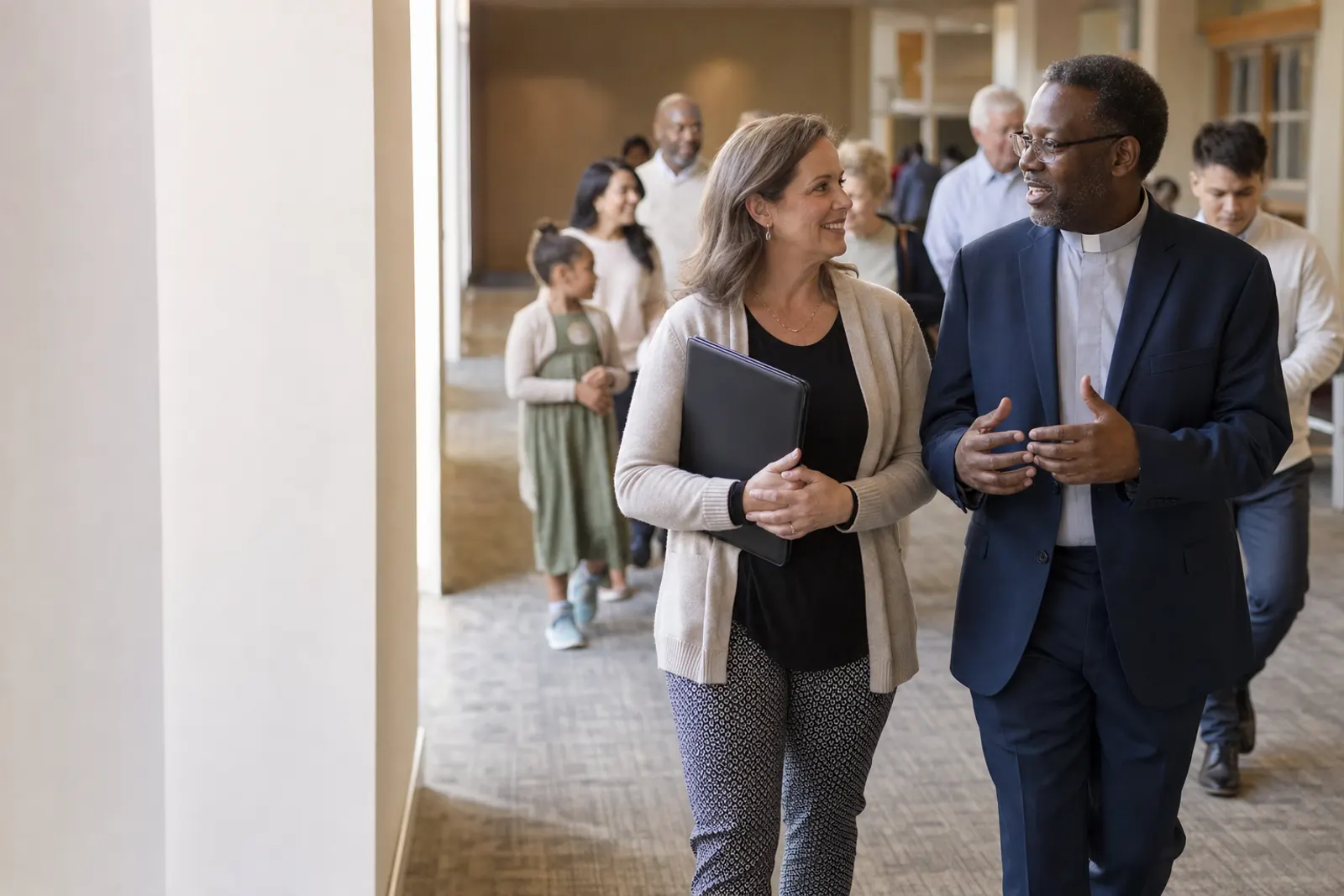 A pastor and the church treasurer talk as they walk down a bright corridor after the service.