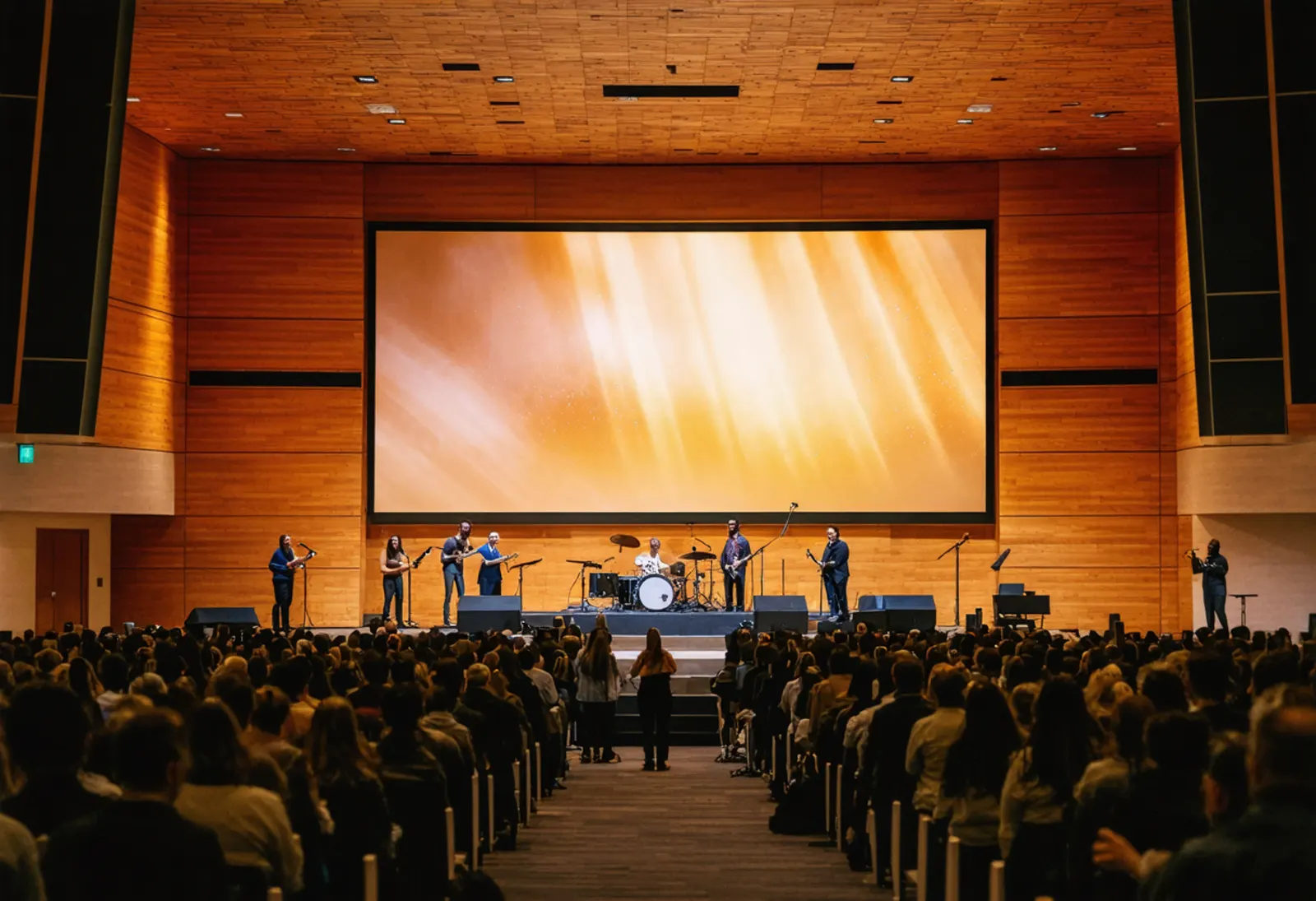The congregation stands in worship in a modern sanctuary as the band leads in front of a large video wall.