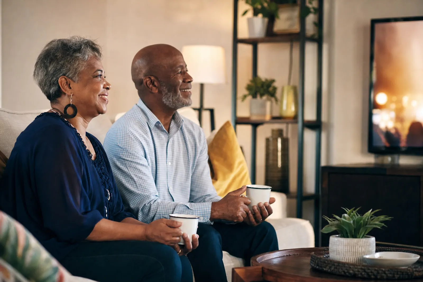 An older couple watches the Sunday service at home with cups of tea.