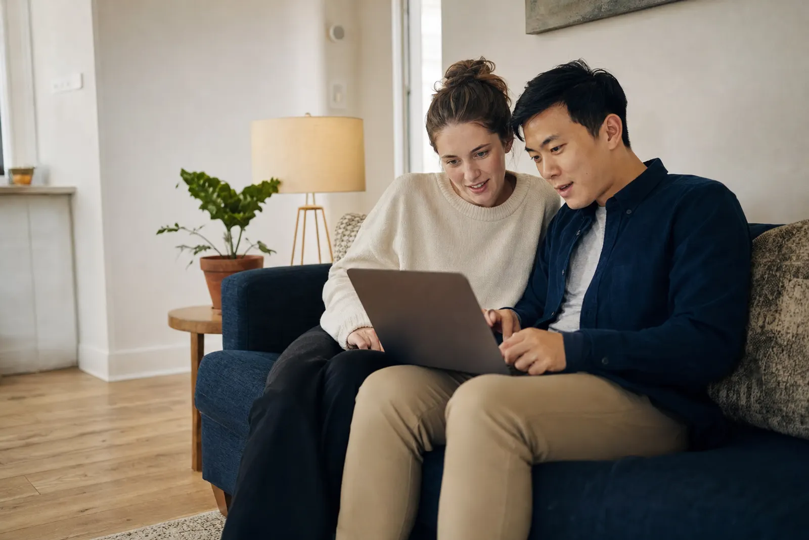 A young couple on their sofa look at a church website together, planning a visit.